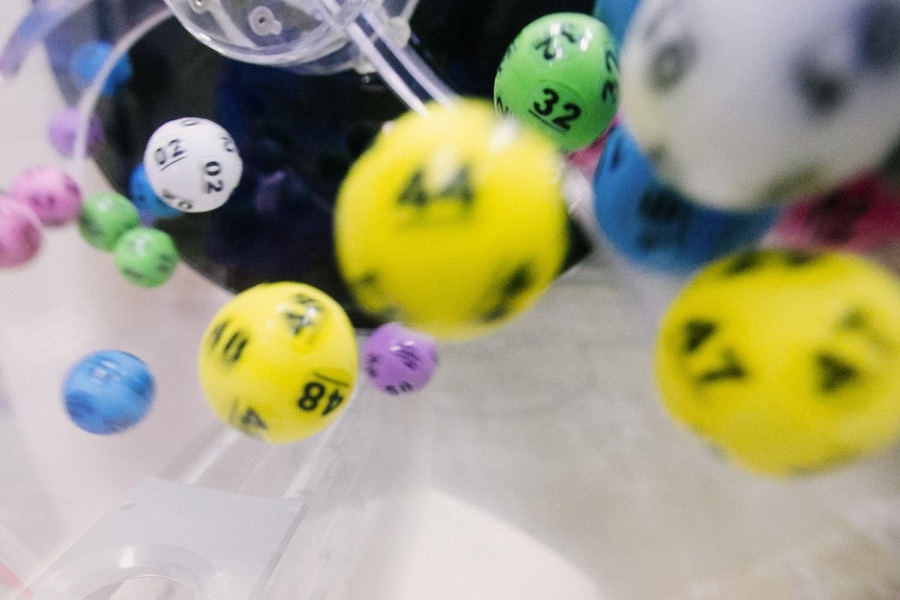 Brightly colored bingo balls in yellow, green, blue, pink, and purple, captured mid-spin in a clear drum.