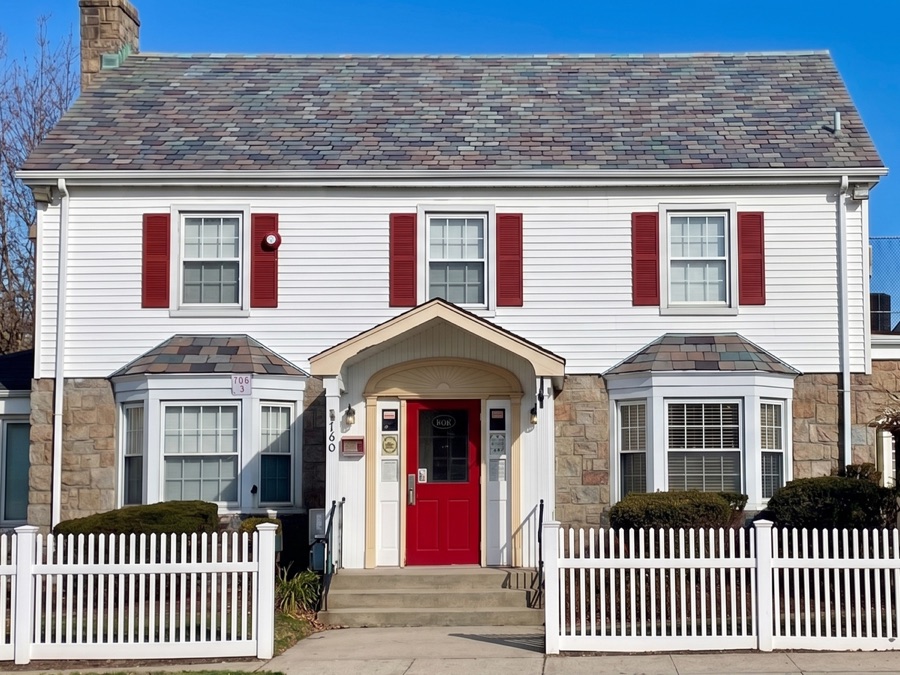 The Rosa Lee Young Childhood Center building — a white colonial-style schoolhouse with red shutters, a red front door, and a white picket fence on a sunny day in Rockville Centre, NY.